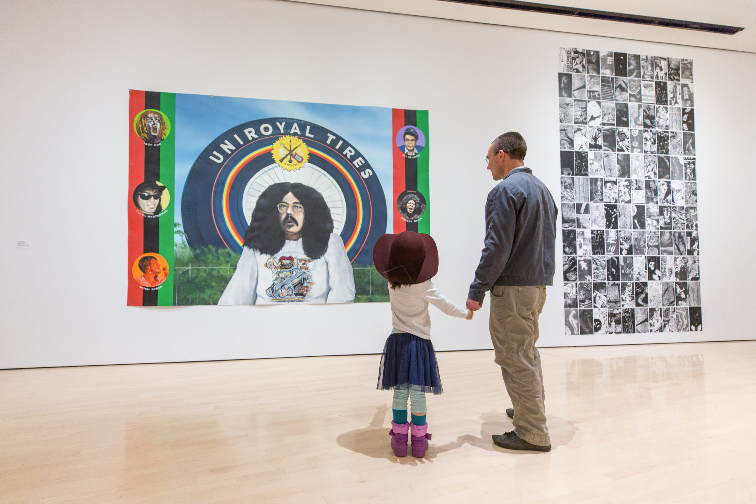 Father and small daughter in large hat look at colorful painting together, holding hands