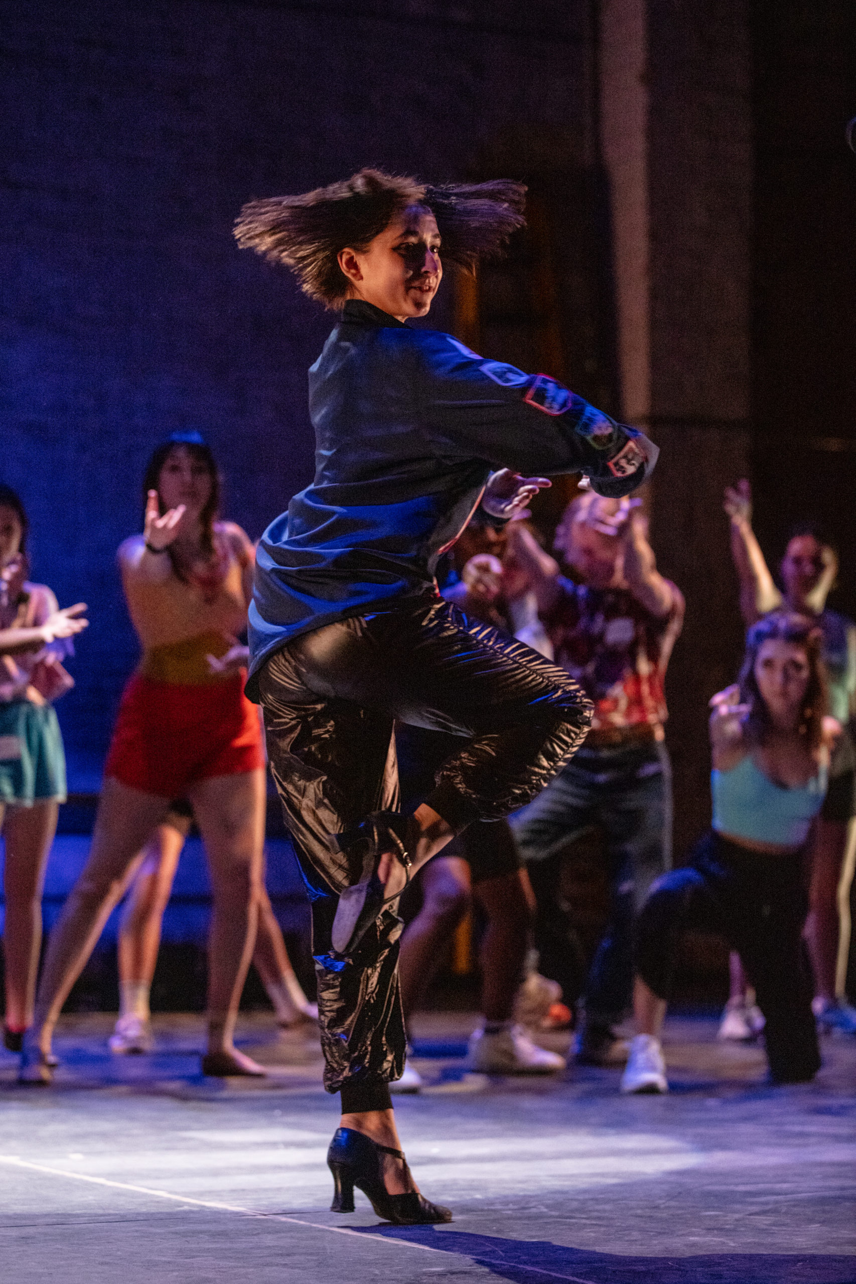 Young woman in blue shirt does pirouette with shoulder length hair spinning on dark purple stage